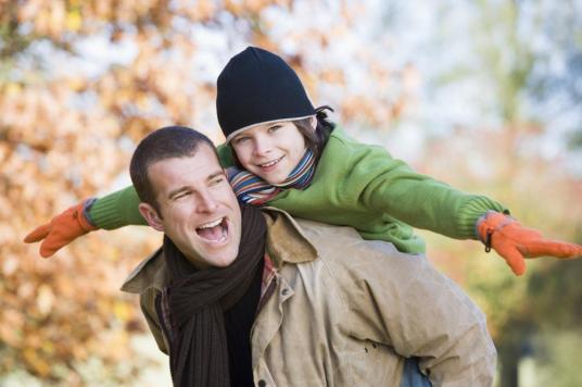 Father piggybacking son outdoors at park and smiling 